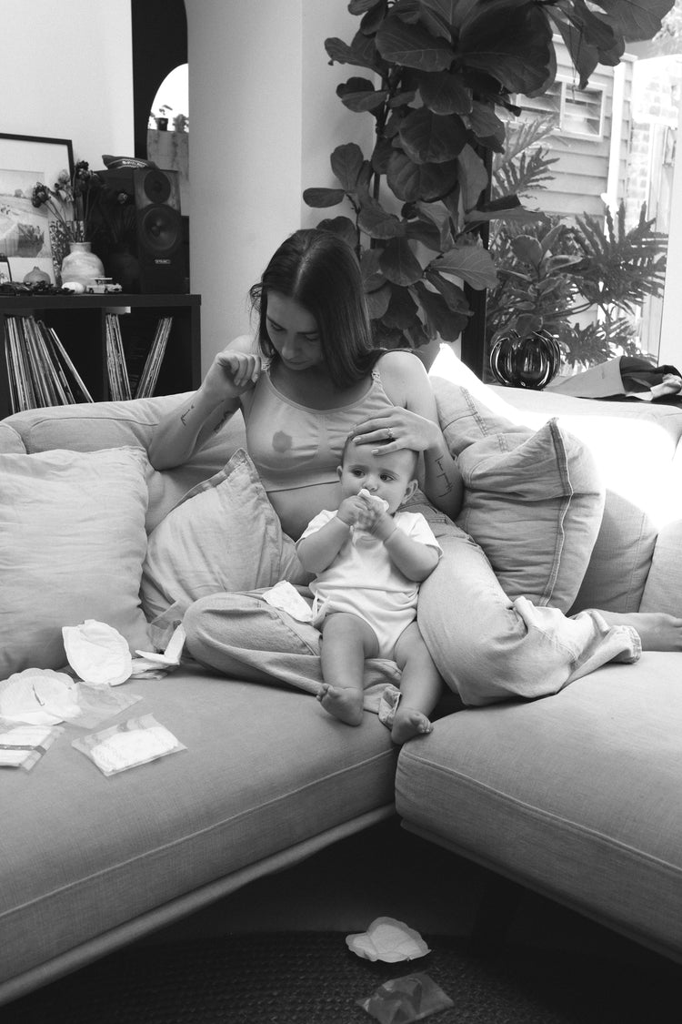 Woman sitting on a couch with a baby on her lap in a home setting.