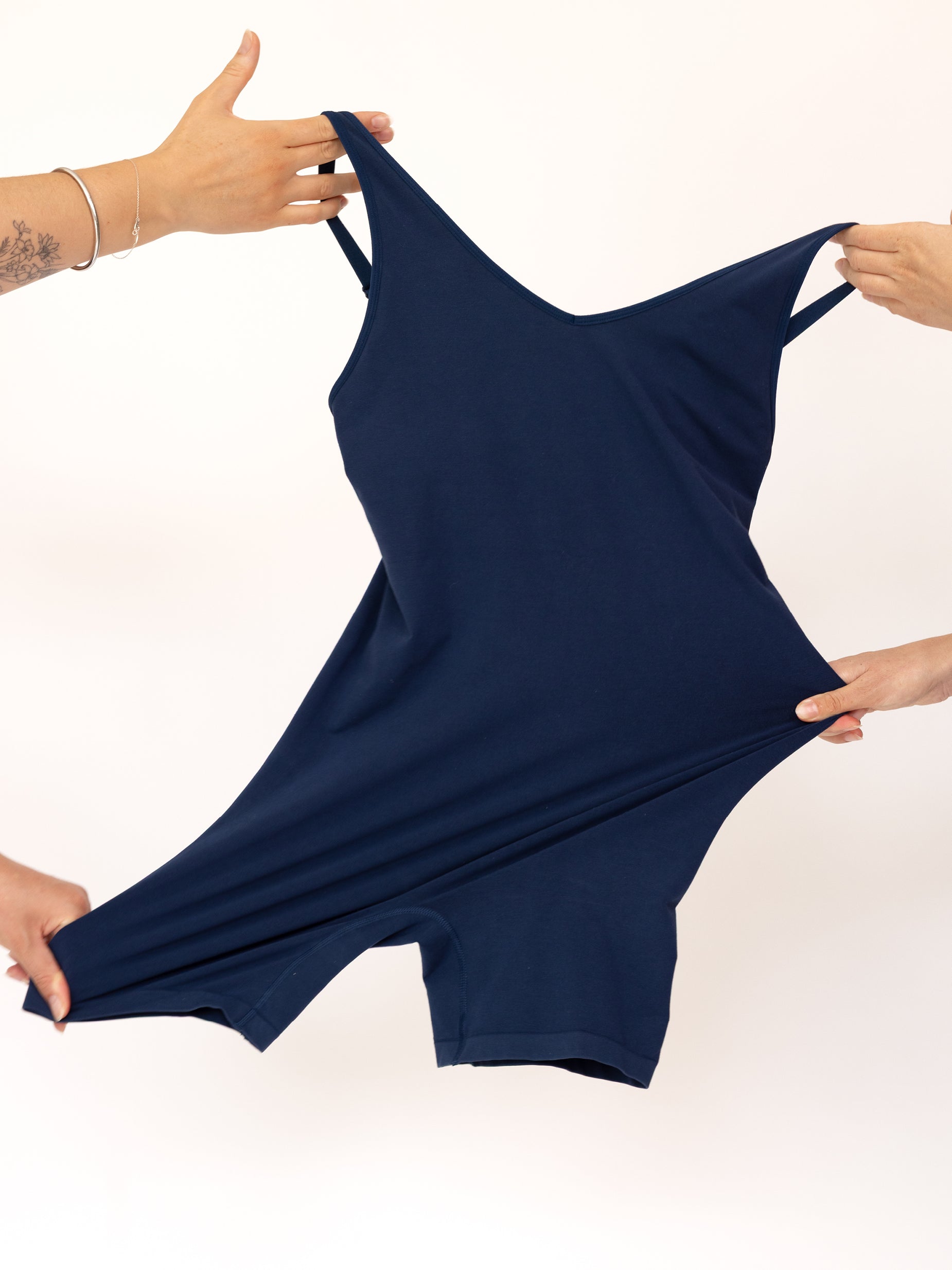 Navy blue bodysuit being stretched by two hands on a white background