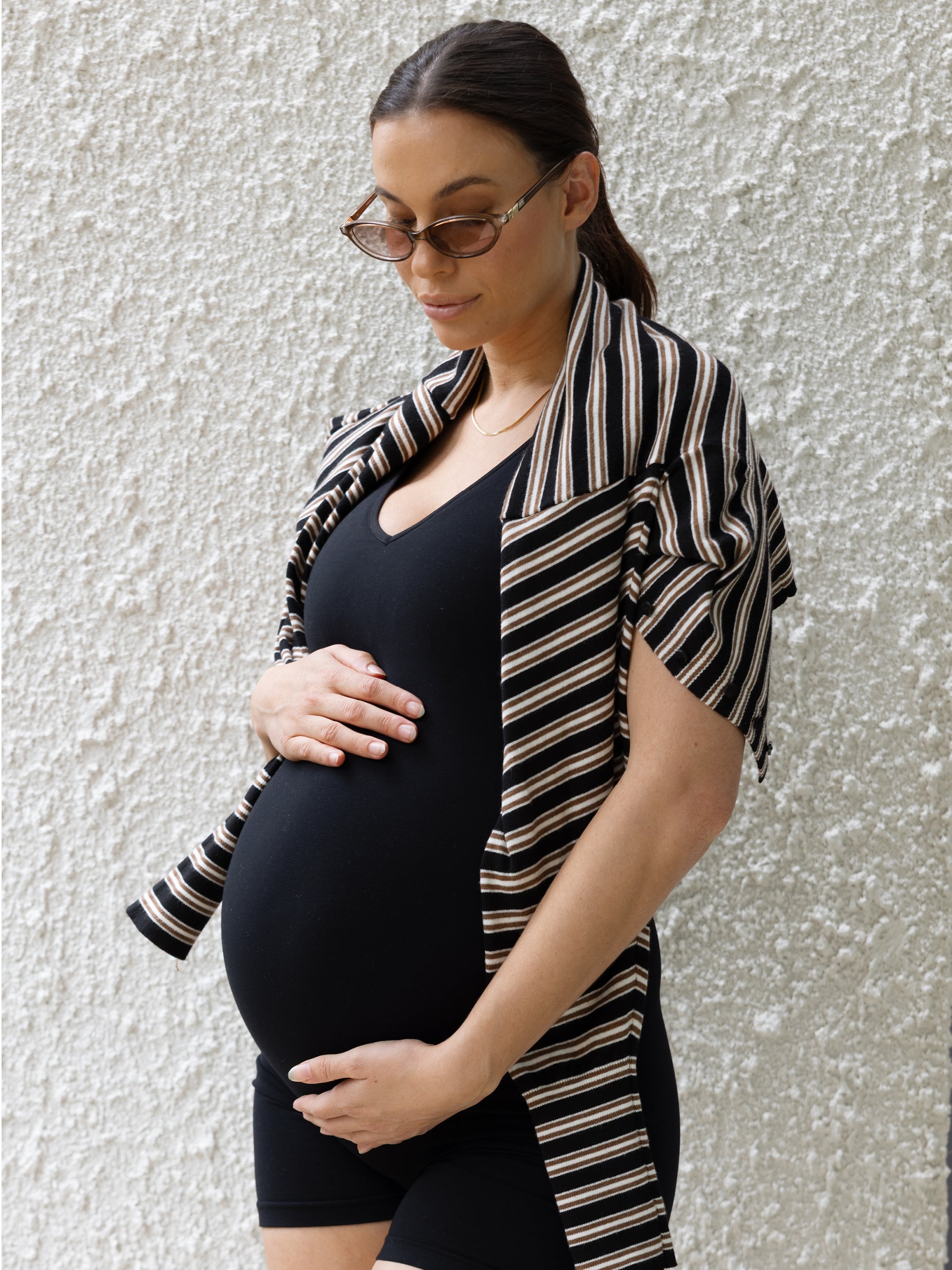 Pregnant woman wearing a black and beige striped cardigan against a textured wall.
