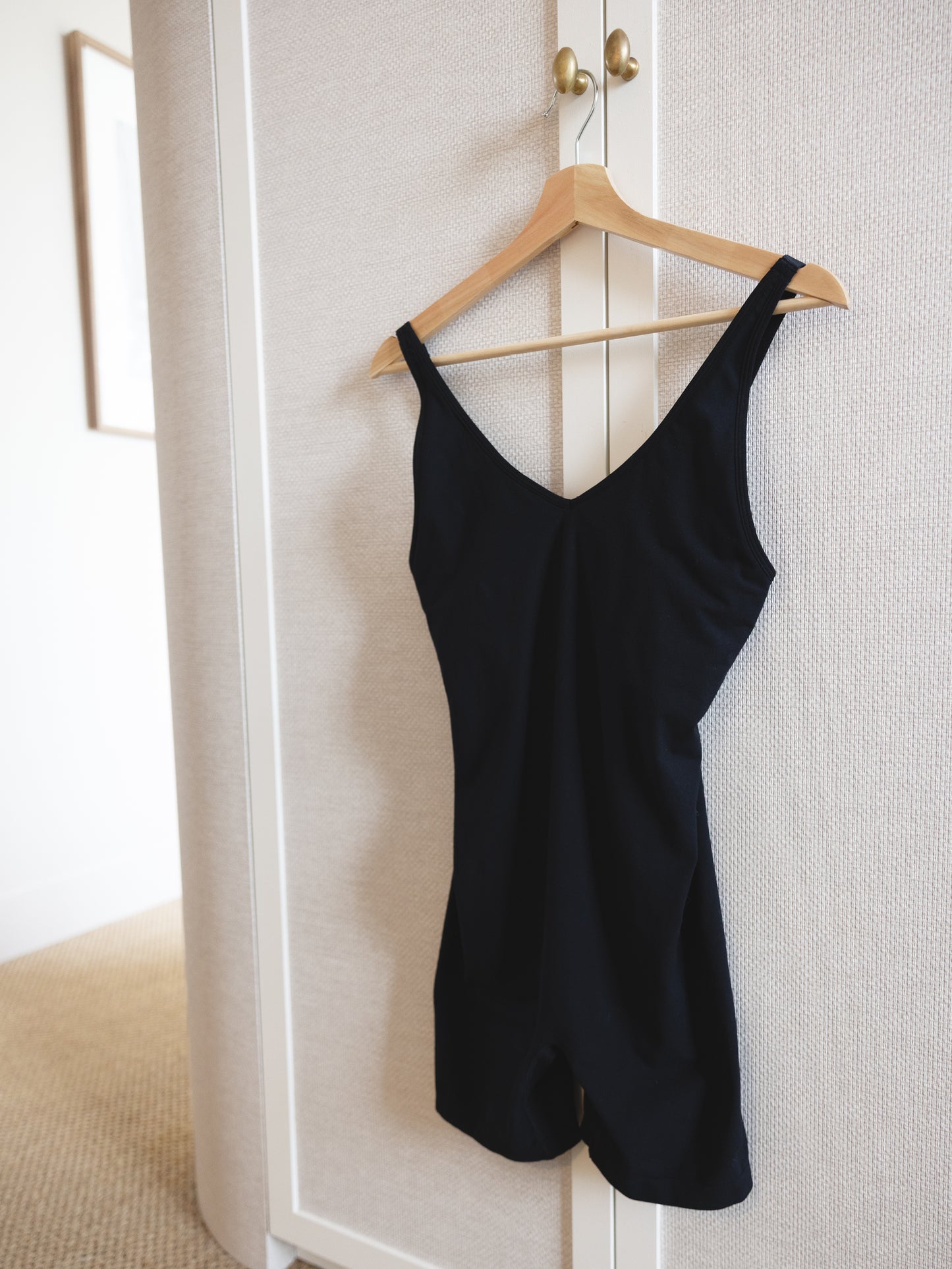 Black bodysuit hanging on a wooden hanger against a white wardrobe door.