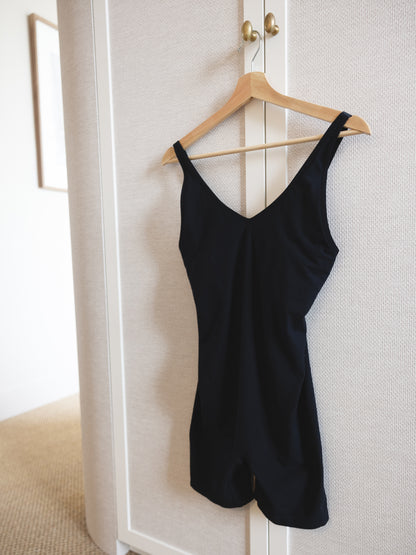 Black bodysuit hanging on a wooden hanger against a white wardrobe door.
