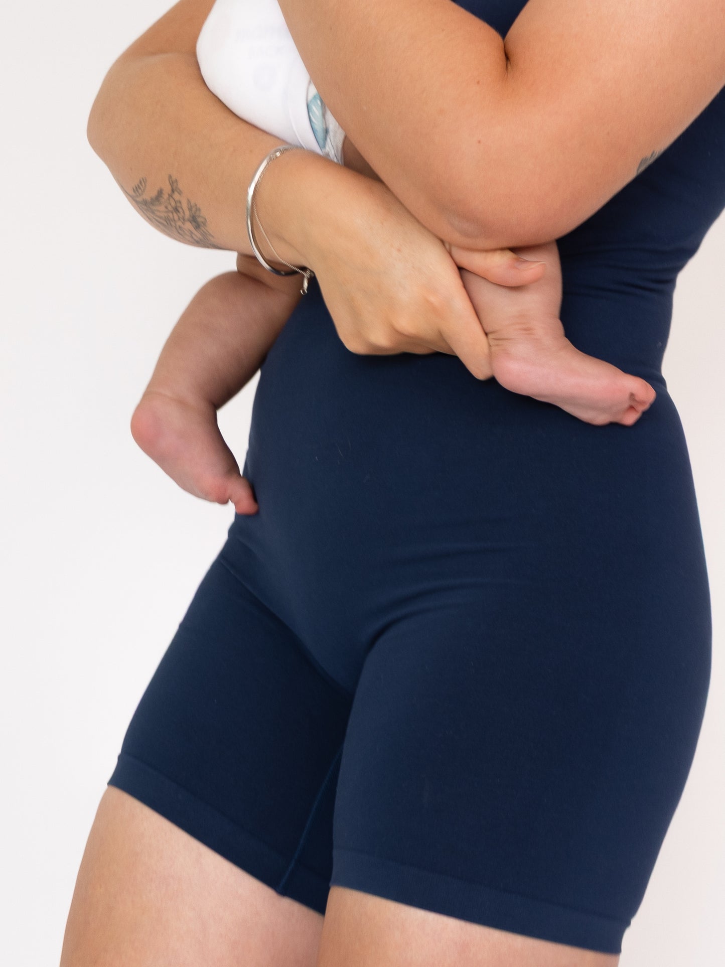 Mum with baby wearing navy blue bodysuit on a plain background